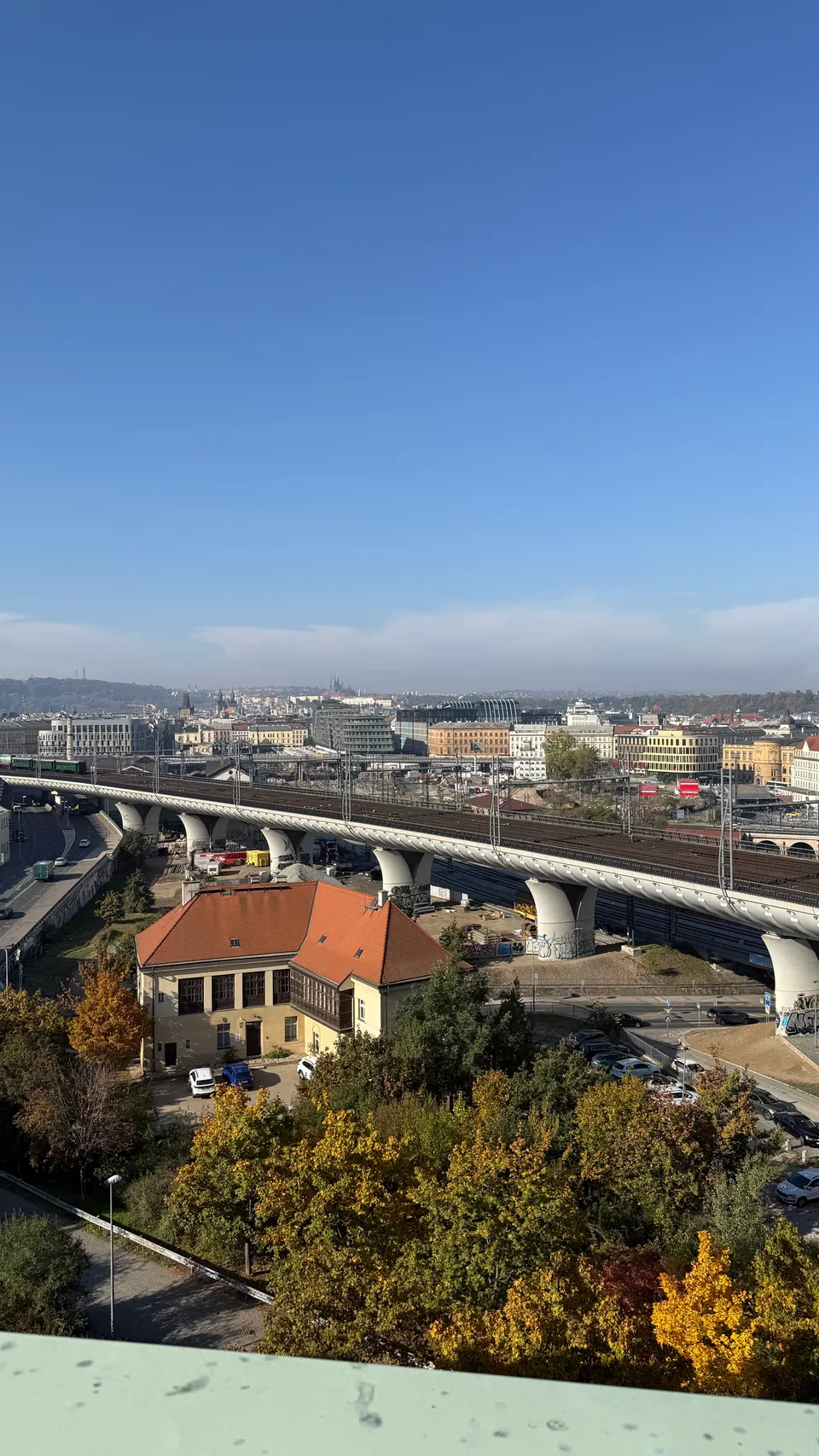 露台正下方：秋天的樹、一棟紅屋頂小房子，還有一座彎彎的高架橋。