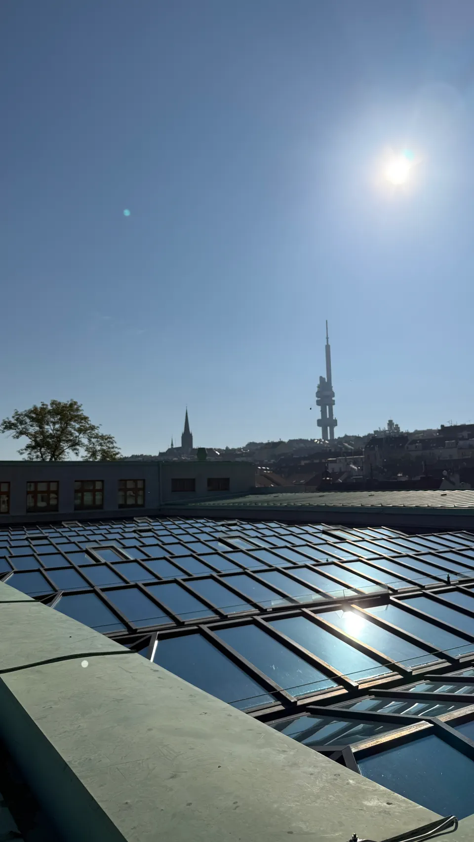 玻璃天窗反射著太陽，遠方是 Žižkov 電視塔。